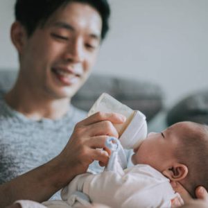 Asian Chinese young father feeding his baby boy son with milk bottle at living room during weekend